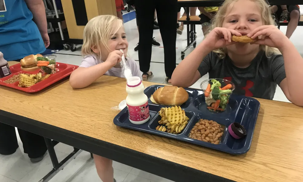 2 students sit a cafeteria table and eat