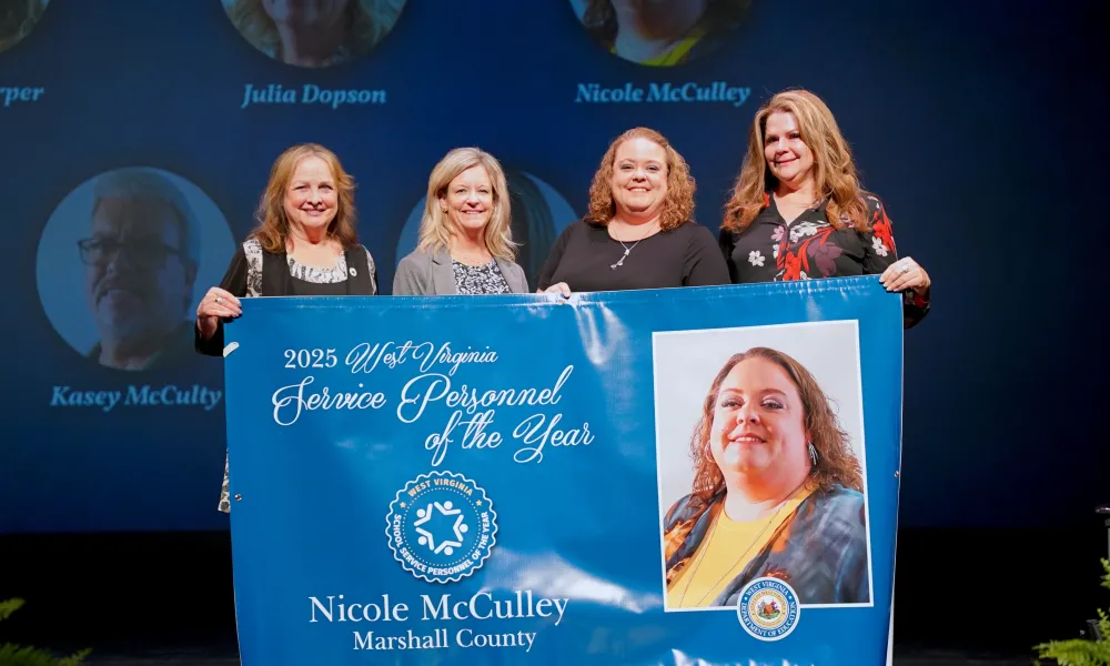 Pictured is Nicole McCulley posing for a group photo while holding a banner.