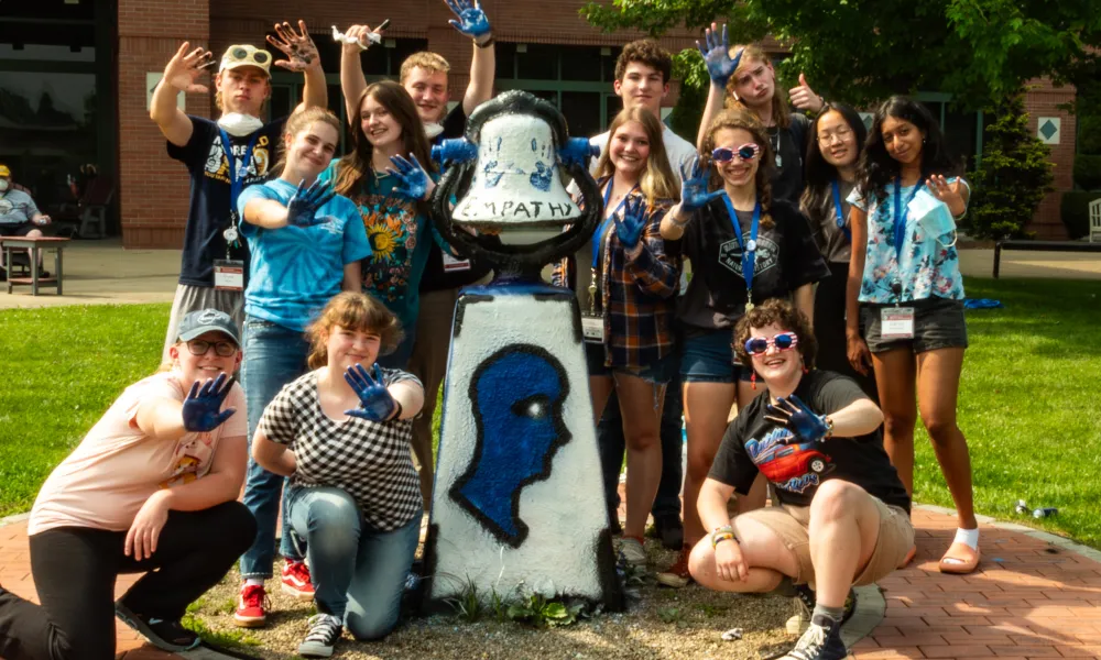 Students gathered together displaying blue painted hands that they are using to decorate a statue on WVU campus