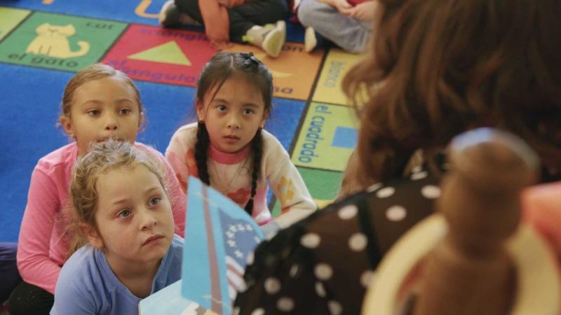 Three elementary students listening to their teacher read a book.