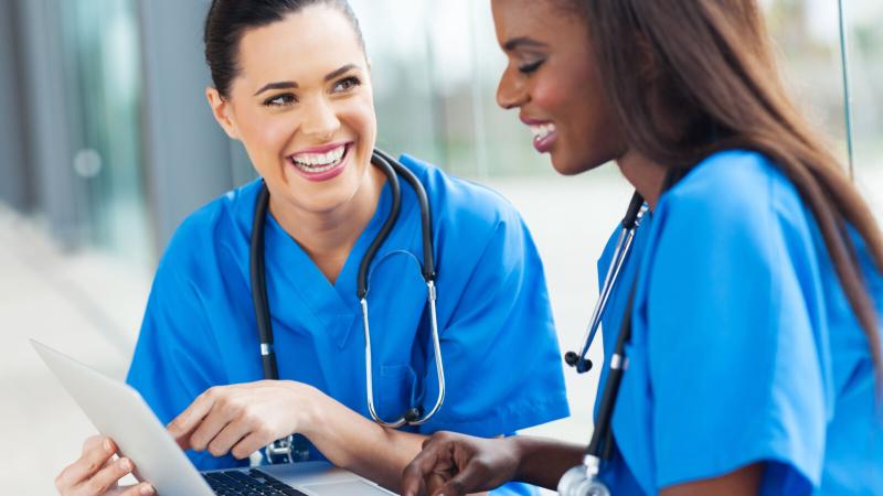 Two female nurses look at a laptop screen and smile.