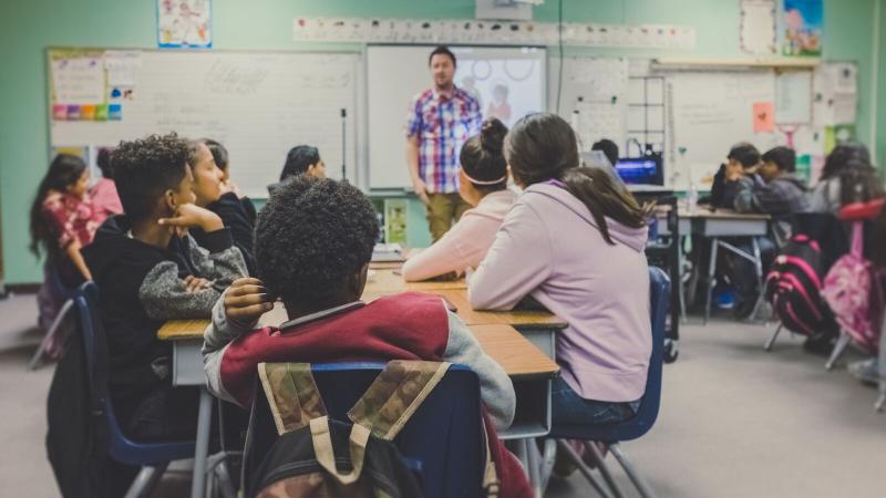 Class of students listening to their teacher speak.