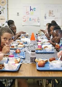 Kids sit at cafeteria table eating