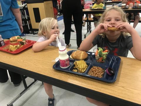 2 students sit a cafeteria table and eat