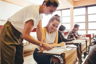 Teacher helping a teenage student at their desk.