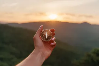 Young woman holding compass in hand in summer mountains at sunrise