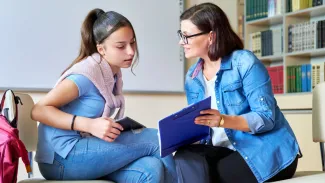 Woman school psychologist teacher mentor talking and helping student, girl teenager, in office near bookcase. Mental health of adolescents, psychology, social issues, professional help of counselor