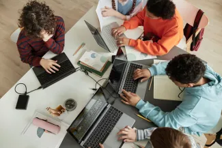 Top view at diverse group of teen school children using computers in classroom studying together at table for Governor's School of Computer Science.