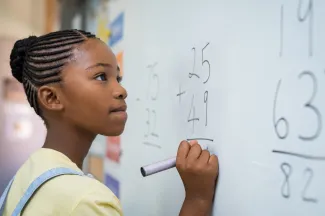 A young female holds a marker while staring with determination at an addition problem on the whiteboard.