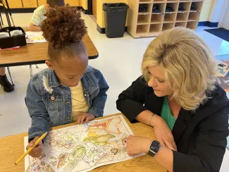 Pictured is Michele Blatt assisting a student sitting at a desk with an activity.