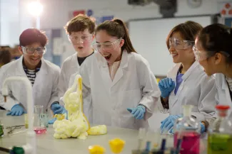 Students dressed in laboratory protective equipment watching an experiment with expanding foam