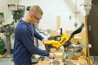 Person standing at a circular saw cutting wood.