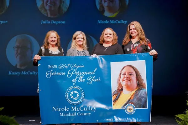 Pictured is Nicole McCulley posing for a group photo while holding a banner.