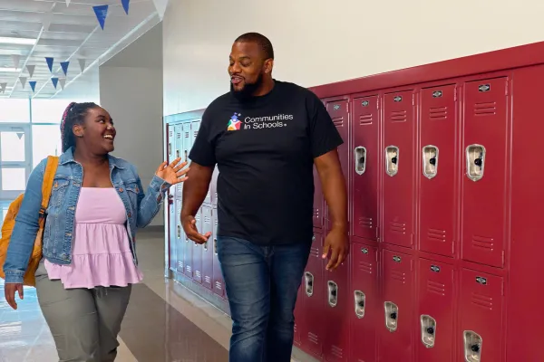 A Communities in Schools coordinator speaks with a student in a school hallway.