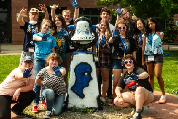 Students gathered together displaying blue painted hands that they are using to decorate a statue on WVU campus